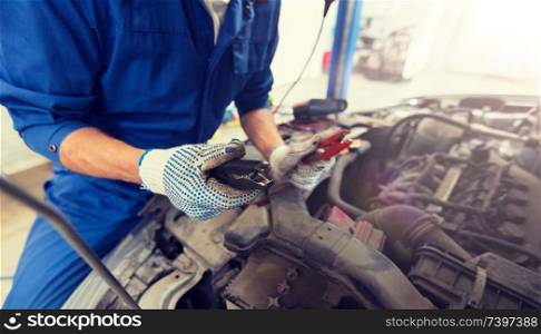 car service, repair, maintenance and people concept - auto mechanic man with cleats charging battery at workshop. auto mechanic man with cleats charging battery