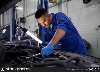 car service, repair, maintenance and people concept - auto mechanic man with lamp working at workshop