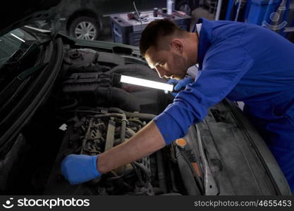 car service, repair, maintenance and people concept - auto mechanic man with lamp working at workshop