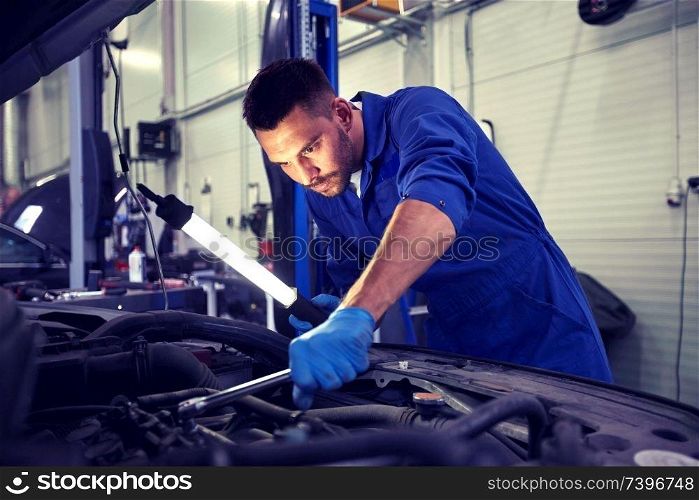 car service, repair, maintenance and people concept - auto mechanic man with lamp working at workshop. mechanic man with lamp repairing car at workshop