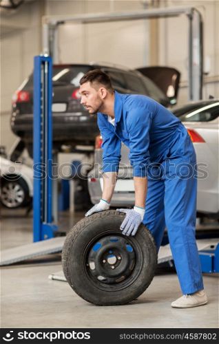 car service, repair, maintenance and people concept - auto mechanic man with wheel tire at workshop
