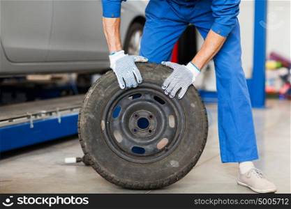car service, repair, maintenance and people concept - auto mechanic man with wheel tire at workshop. mechanic with wheel tire at car workshop