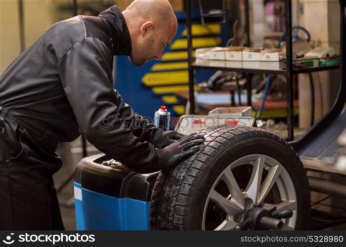 car service, repair, maintenance and people concept - auto mechanic man working with wheel balancing machine at workshop. auto mechanic balancing car wheel at workshop