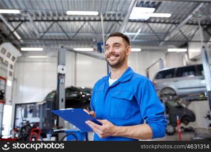 car service, repair, maintenance and people concept - happy smiling auto mechanic man or smith with clipboard at workshop