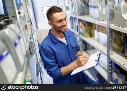 car service, repair, maintenance and people concept - smiling auto mechanic man or smith writing to clipboard at workshop or warehouse
