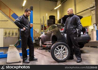 car service, repair, maintenance and people concept - two auto mechanics changing tires at workshop. auto mechanics changing car tires at workshop