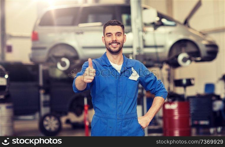 car service, repair, maintenance, gesture and people concept - happy smiling auto mechanic man or smith showing thumbs up at workshop. happy auto mechanic man or smith at car workshop