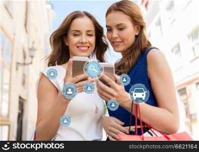 car sharing, modern technology and people concept - happy young women with shopping bags and smartphones on city street. women shopping and using car sharing on smartphone