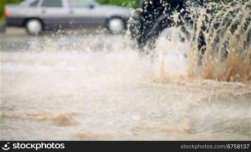 car splashes through a large puddle on a wet urban road