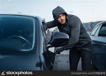 Car thief breaking door, criminal job, burglar, stealing. Hooded male robber opening vehicle on parking. Auto robbery, automobile crime. Car thief breaking door, criminal job, burglar