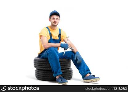 Car tire service, worker in blue uniform sitting on car tyres, white background, repairman, wheel mounting