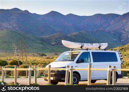 Car van with canoe on top roof against mountain nature. Cabo de Gata Nijar Natural Park, province Almeria, Andalusia in Spain. Active lifestyle sports concept.. Canoe on roof top of car against mountain