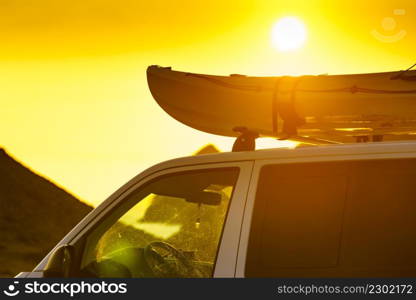 Car van with canoe on top roof against sunset sky. Active lifestyle, vanlife concept.. Canoe on roof top of car van at sunset