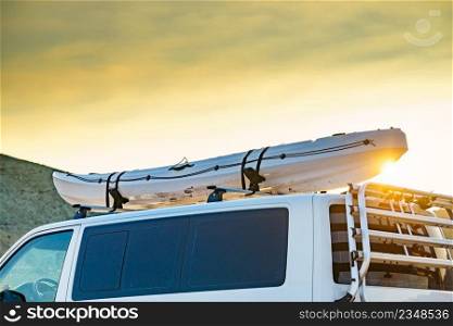Car van with canoe on top roof against sunset sky. Active lifestyle, vanlife concept.. Canoe on roof top of car van at sunset