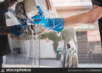 Car wash staff wearing blue rubber gloves using a sponge moistened with soap and water to clean the car.