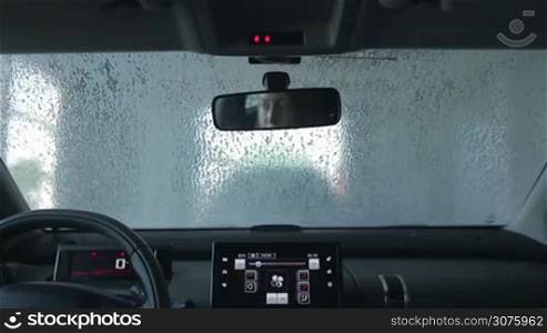 Car wash with pressured water at service station. Automatic car cleaning in action. View inside of car&acute;s cab