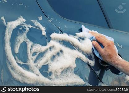 Car washing with a blue sponge. Female hand washes the machine with soap foam. Toning. Car washing with a blue sponge