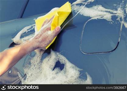 Car washing with a yellow sponge. Female hand washes the machine with soap foam. Car washing with a yellow sponge