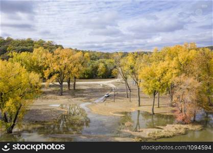 car with a boat of roof on a muddy shore of the flooded Missouri River at Brownville, Nebraska, covering a boat ramp, fall colors scenery with cottonwood tress, aerial perspective
