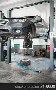 Car with removed wheel on the lift, nobody. Automobile repair, vehicle maintenance, tire service. Car with removed wheel on the lift, nobody