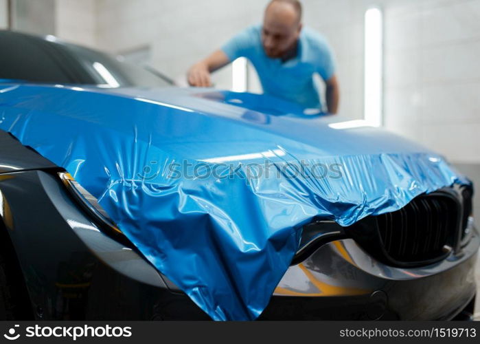 Car wrapping, man installs protective vinyl foil or film on hood. Worker makes auto detailing. Automobile paint protection coating, professional tuning. Car wrapping, man installs protective vinyl foil