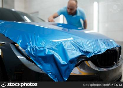 Car wrapping, man installs protective vinyl foil or film on hood. Worker makes auto detailing. Automobile paint protection coating, professional tuning. Car wrapping, man installs protective vinyl foil