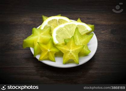 Carambola and lemon on dark brown wooden background.
