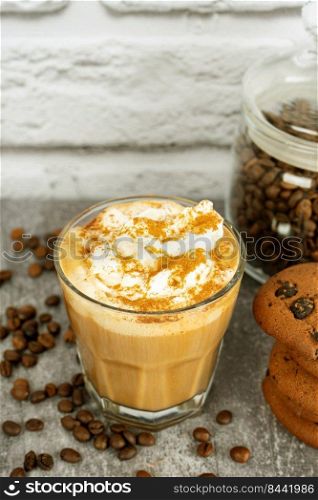 Caramel latte coffee in a glass with whipped cream and chocolate cookie. Coffee beans on gray and white brick wall surface with copy space.. Iced caramel latte coffee in a glass with syrup and whipped cream.