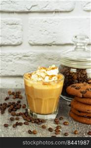 Caramel latte coffee in a glass with whipped cream and chocolate cookie. Coffee beans on gray and white brick wall surface with copy space.. Iced caramel latte coffee in a glass with syrup and whipped cream.