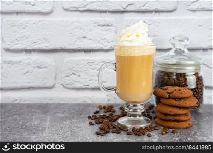 Caramel latte coffee in a tall glass with whipped cream and chocolate cookie. Coffee beans on gray and white brick wall surface with copy space.. Iced caramel latte coffee in a tall glass with syrup and whipped cream.