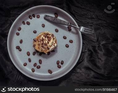 Caramel Pecanbon topped with decadent caramel frosting and pecans served with Coffee beans and Metal fork on ceramic plate with dark background. Top view, Space for text, Selective focus.