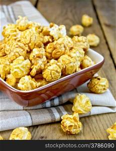 Caramel popcorn in a clay bowl with a napkin on a wooden boards background