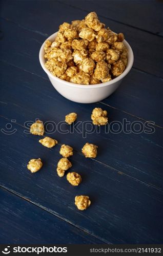 Caramel Popcorn in white bowl on rustic blue wooden table. Close up. Copy space for your text