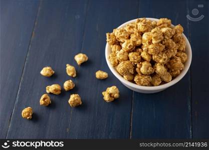 Caramel Popcorn in white bowl on rustic blue wooden table. Close up. Copy space for your text