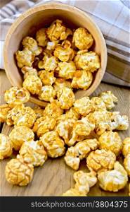 Caramel popcorn poured out of wooden bowls, napkin on the background of wooden boards