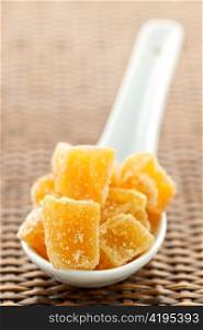 Caramelized ginger candy pieces on white spoon close up