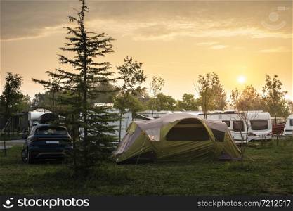 Caravans and tent on green meadow in campsite. Sunrise, rays on campers and tent in the morning. Green grass. Outdoor concept for traveling and res in the nature.