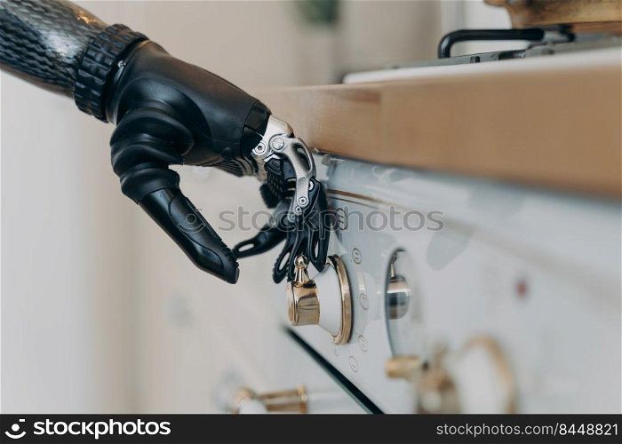 Carbon prosthetic hand of disabled person is switching a stove on at kitchen. Amputee with high technology artificial arm at home. Functions of modern bionic prosthesis. Routine of disabled person.. Carbon prosthetic hand of disabled is switching a stove on at kitchen. Routine of disabled person.