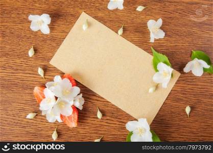 card on a wooden surface with jasmine flowers and strawberries. background