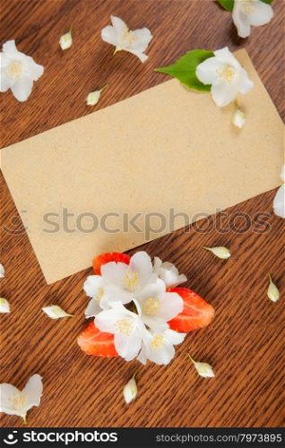 card on a wooden surface with jasmine flowers and strawberries. background
