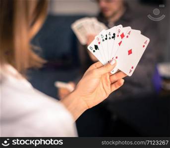 Card playing at home: Friends are sitting on a table. Woman playing cards, man in blurry background.