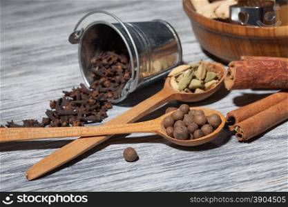Cardamon, clove and pepper in spoons on wooden background with various spices - cinnamon, ginger and nutmeg
