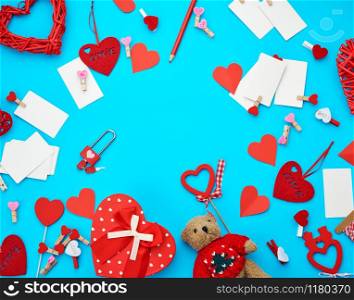 cardboard boxes in the form of a heart, a small teddy bear, white blank business cards with clothespins on a blue background, decor and objects for Valentine&rsquo;s Day, flat lay, copy space
