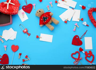 cardboard boxes in the form of a heart, a small teddy bear, white blank business cards with clothespins on a blue background, decor and objects for Valentine&rsquo;s Day, flat lay, copy space