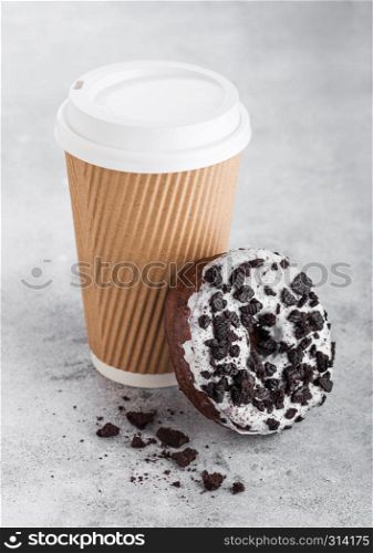 Cardboard coffee cup with black cookies doughnut on stone kitchen background. Cafe drink and snack.