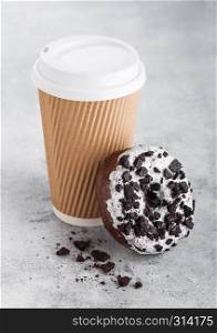 Cardboard coffee cup with black cookies doughnut on stone kitchen background. Cafe drink and snack.