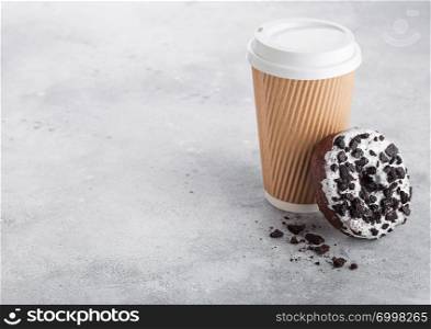 Cardboard coffee cup with black cookies doughnut on stone kitchen table background. Cafe drink and snack.