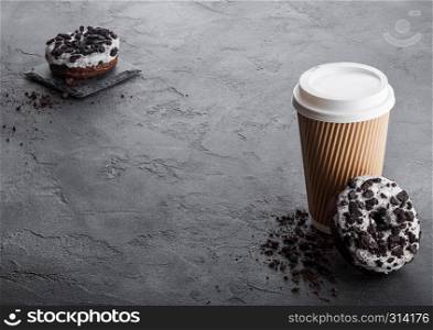 Cardboard coffee cup with black cookies doughnuts on black stone kitchen table background. Cafe drink and snack.