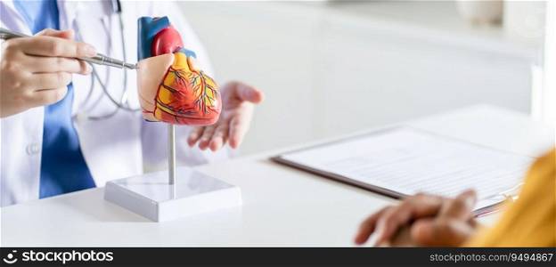 Cardiology Consultation treatment of heart disease. Doctor cardiologist while consultation showing anatomical model of human heart with aged patient talking about heart diseases