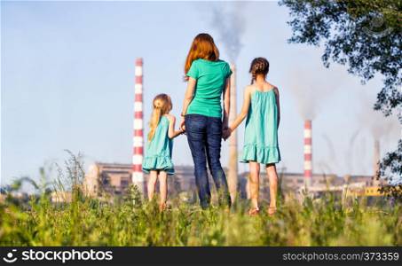 care future concept. Young mother with her kids are looking at the chimney-stalks polluting an air